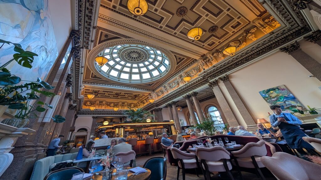 The stunning, high-ceilinged dining room of The Spence restaurant inside the Gleneagles Townhouse, featuring grand stone pillars and a central bar.